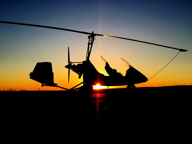 A gyroplane silhouetted against the setting sun