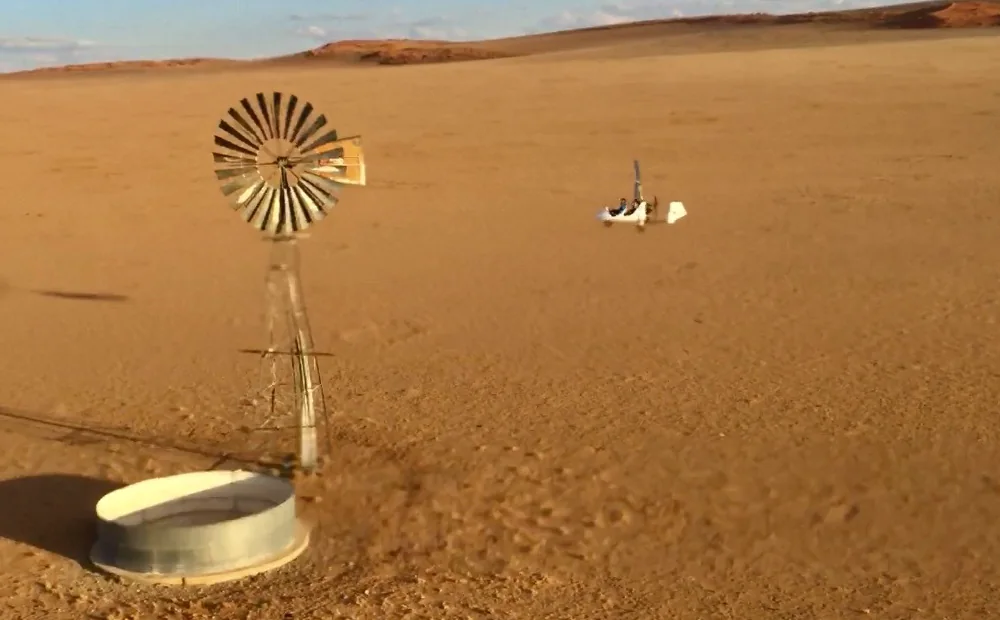 A wind pump turning in the Namib, with a gyroplane in flight beyond it